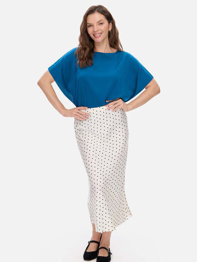 A woman modeling a two-piece outfit consisting of a bright blue short-sleeve silk top and a white midi skirt with black polka dots, set against a plain light gray background.