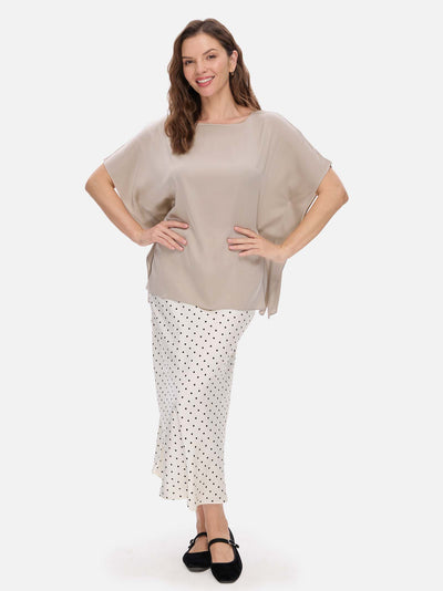 Woman wearing a beige silk top and white polka dot skirt on a white background