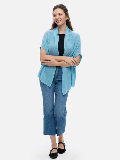 Woman wearing a light blue cashmere vest over a black top and blue jeans on a white background