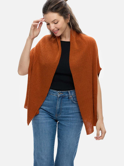 Woman wearing a rust-colored cashmere vest over a black top and blue jeans on a white background