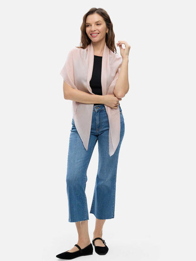 Woman wearing a blush Square Featherlight Cashmere Scarf wrapped around her neck and shoulders with a black sleeveless top and blue jeans.