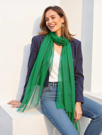 Woman wearing a green scarf, blue blazer, and jeans sitting on a white chair.