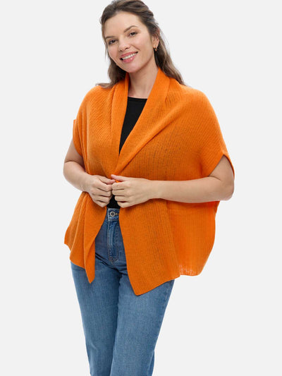 Woman wearing an orange cashmere vest over a black top and blue jeans on a white background