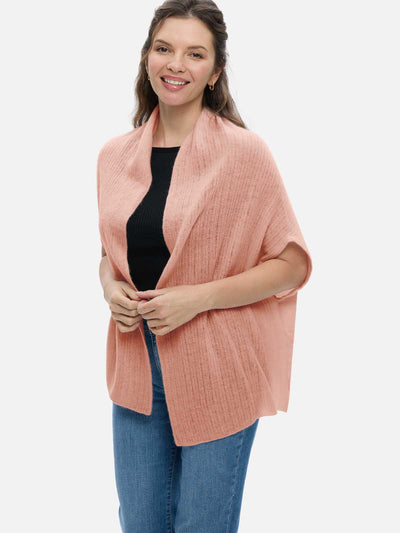 Woman wearing a pink knitted cashmere vest over a black top and blue jeans on a white background