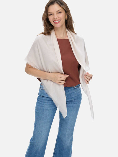Woman wearing an Ivory Square Featherlight Cashmere Scarf draped over her shoulders, styled with a rust-brown top and blue jeans.