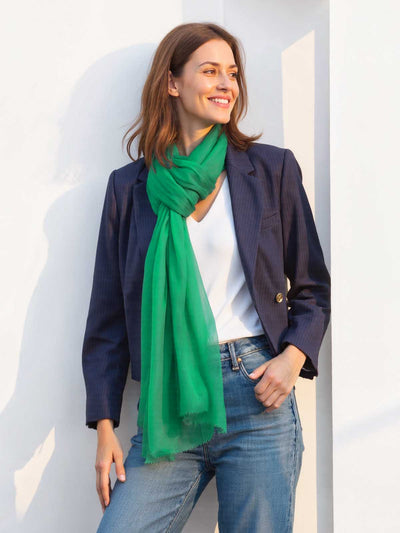 Woman wearing a green scarf, navy blazer, white shirt, and jeans against a white wall.