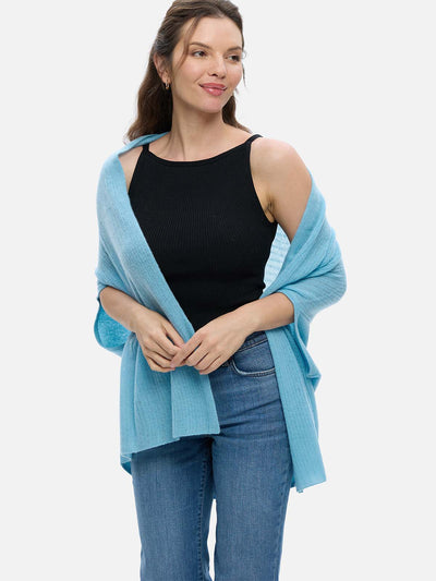 Woman wearing a light blue cashmere vest over a black top and jeans on a white background