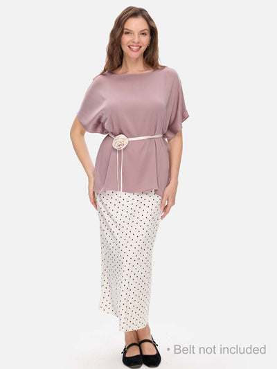 Woman wearing a mauve silk top and white polka dot skirt on a white background