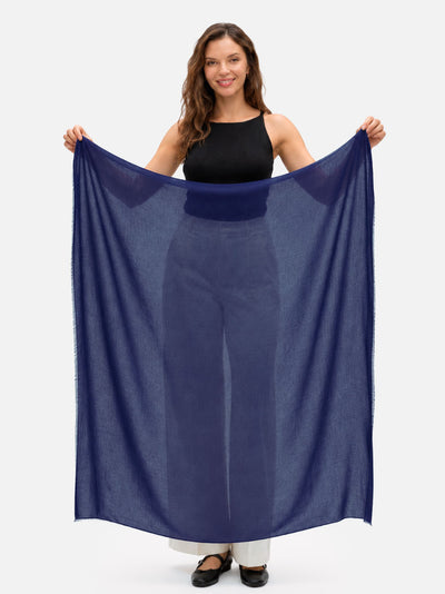 Woman holding a navy blue Featherlight Square Cashmere Scarf fully open to show its generous square shape, lightweight weave, and sheer finish.