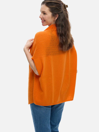 Woman wearing an orange cashmere vest and blue jeans on a white background