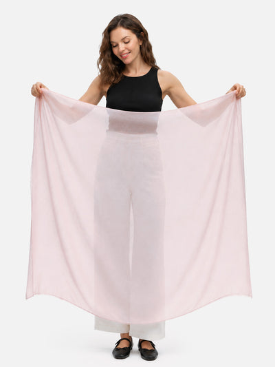 A woman modeling a large, lightweight, semi-sheer featherlight blush cashmere scarf, holding it wide open against a plain white studio background.