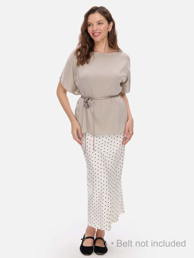 Woman wearing a beige silk top and polka dot skirt on a white background