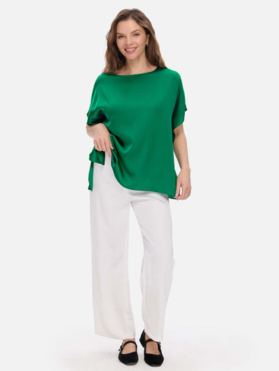 Woman wearing a green silk top and white pants on a white background