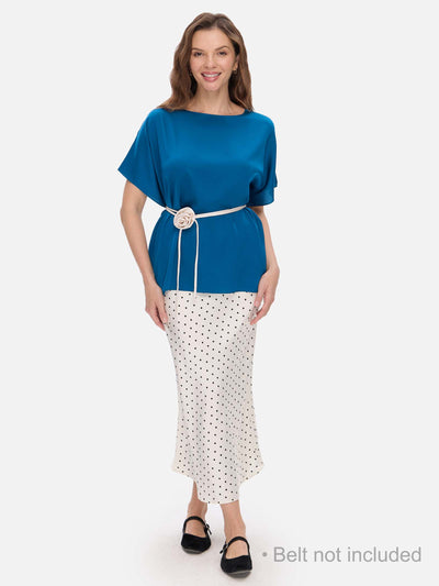 A woman modeling a two-piece outfit consisting of a short-sleeve blue silk top and a white midi skirt with black polka dots. The top is cinched at the waist with a white belt featuring a decorative flower detail.