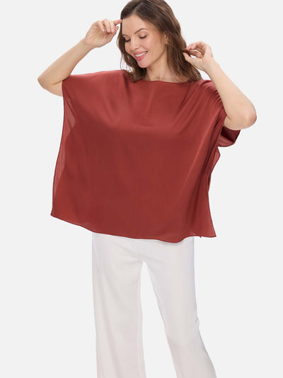 Woman wearing a rust-colored silk top and white pants on a white background