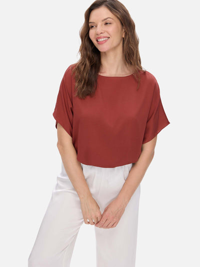Woman wearing a rust-colored silk top and white pants on a light gray background