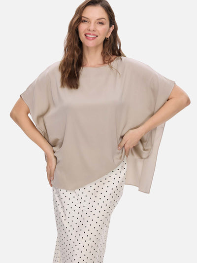 A woman modeling a loose, short-sleeve taupe silk top paired with a white skirt featuring black polka dots, set against a solid light gray background.