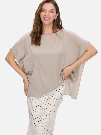 Woman wearing a beige silk top and polka dot pants on a white background