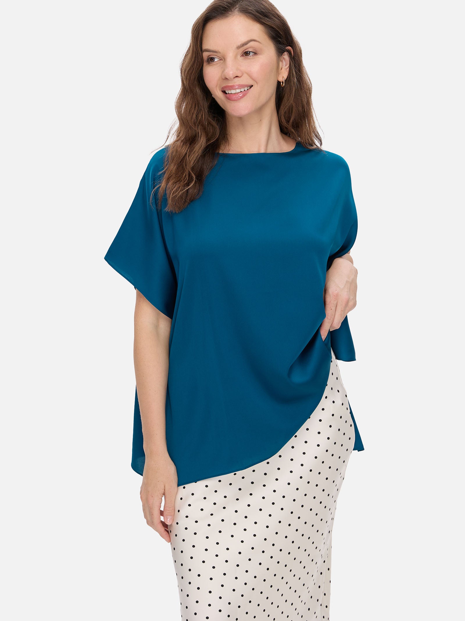 Woman wearing a teal silk top and polka dot skirt on a white background