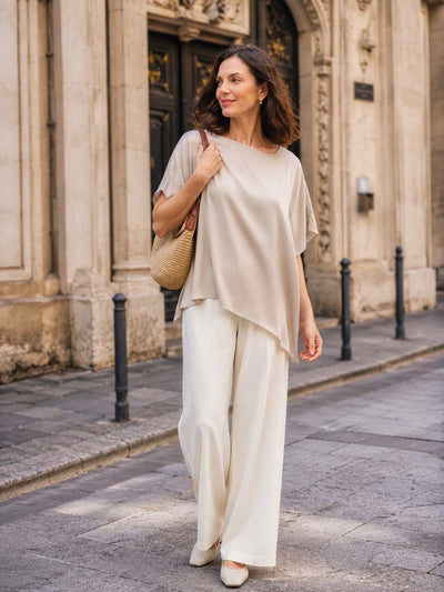 Woman in a beige silk top and white pants walking on a street.