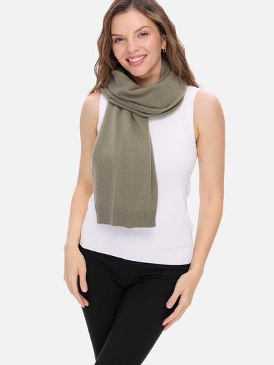 Woman wearing a green scarf, white top, and black pants on a white background