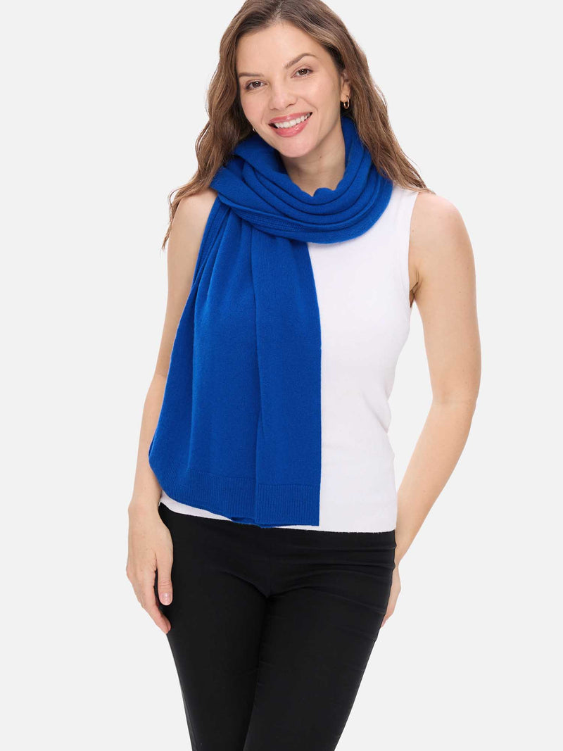 Woman wearing a blue cashmere wrap over a white top and black pants on a white background