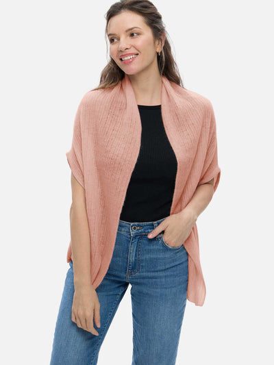 Woman wearing a pink cashmere vest, black top, and blue jeans on a white background
