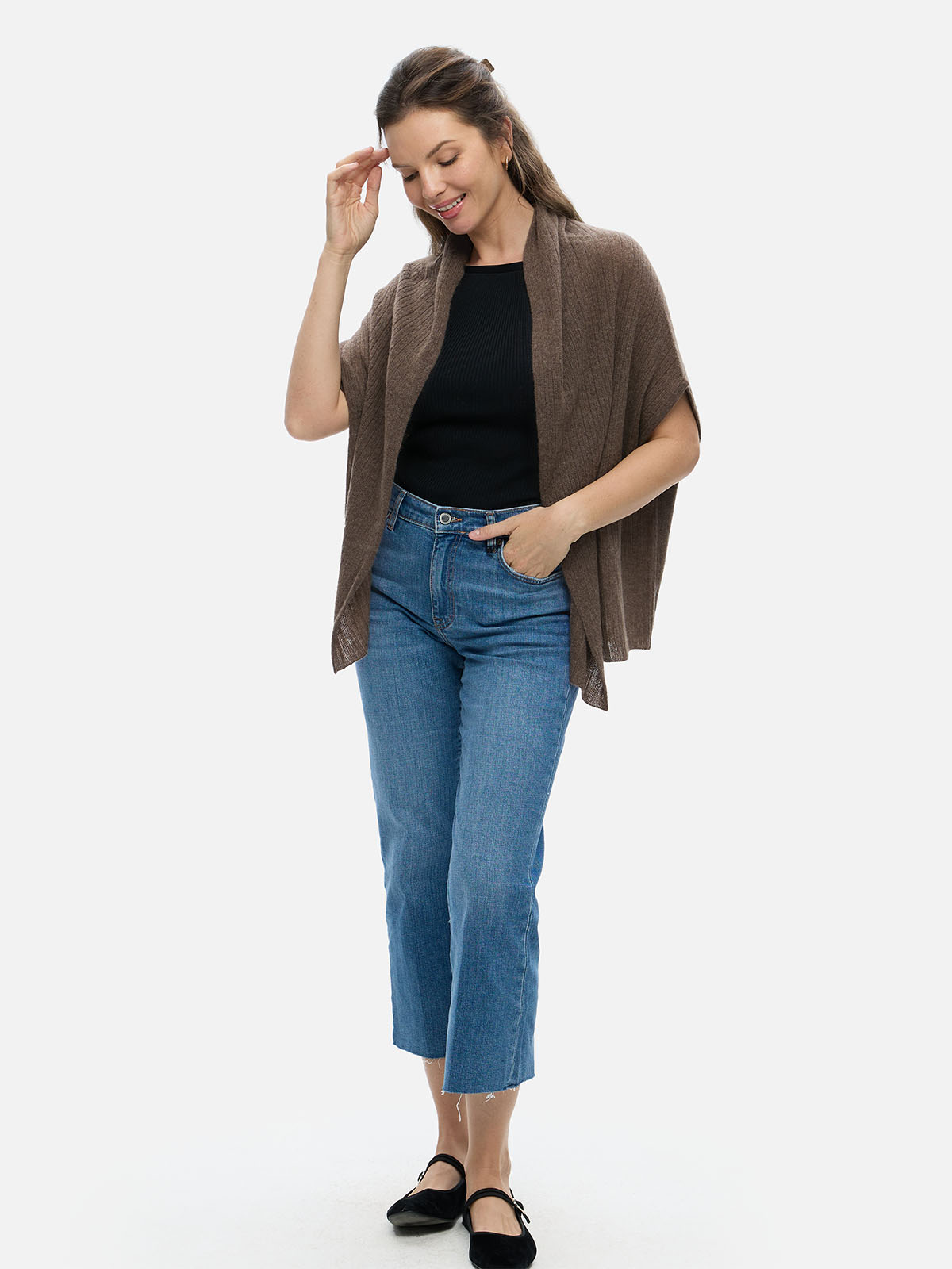 Woman wearing a brown cashmere vest, black top, and blue jeans on a white background