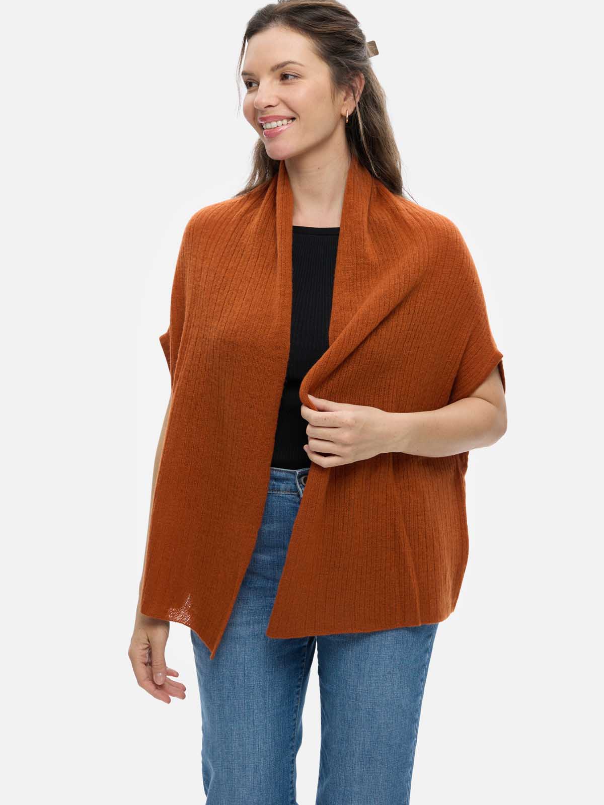Woman wearing a rust-colored cashmere vest over a black top and blue jeans on a white background