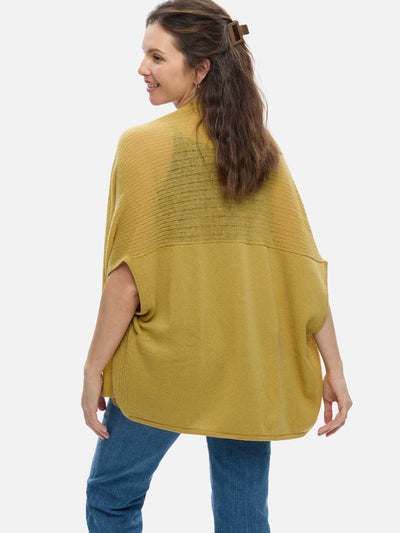 Woman wearing a mustard yellow cashmere vest over a blue top on a white background