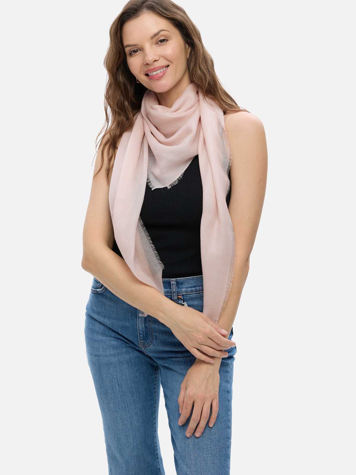 Woman wearing a blush Square Featherlight Cashmere Scarf wrapped around her neck and shoulders with a black sleeveless top and blue jeans.