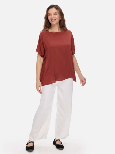 Woman wearing a rust-colored silk top and white pants on a white background