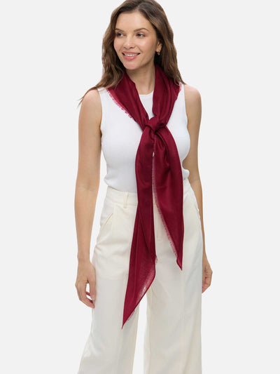 Woman wearing a wine red Ovcio Featherlight Cashmere Scarf over a white top and ivory trousers.