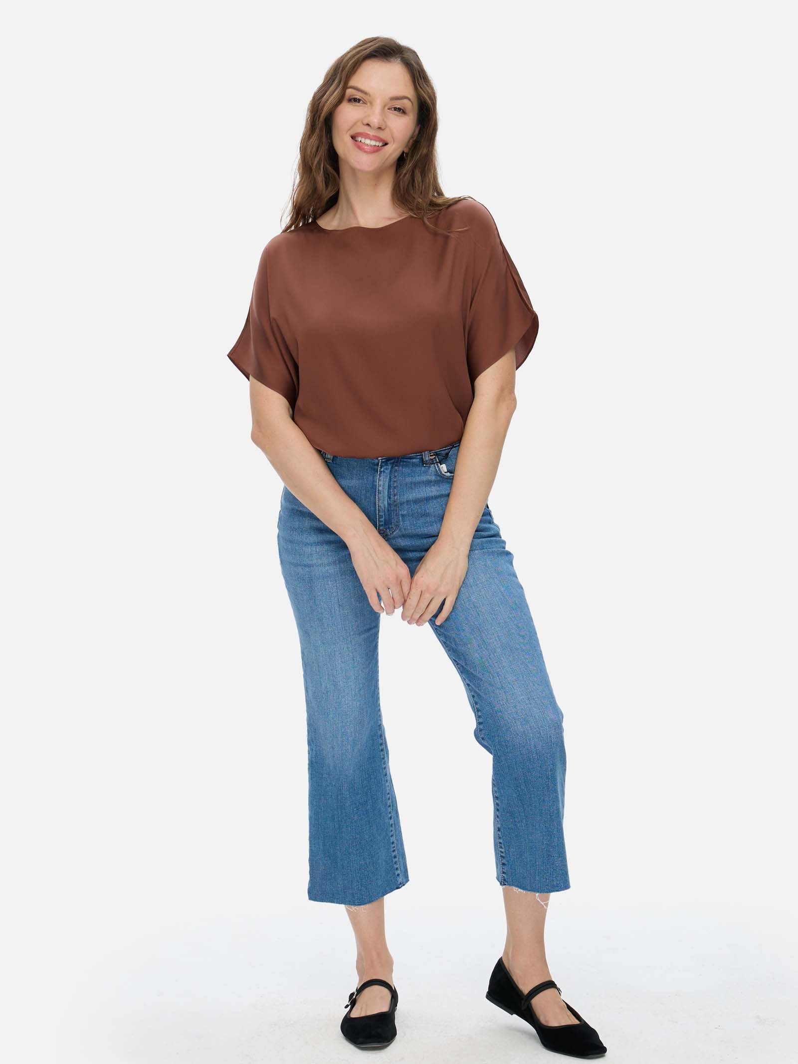 Woman wearing a brown silk top and blue jeans on a white background