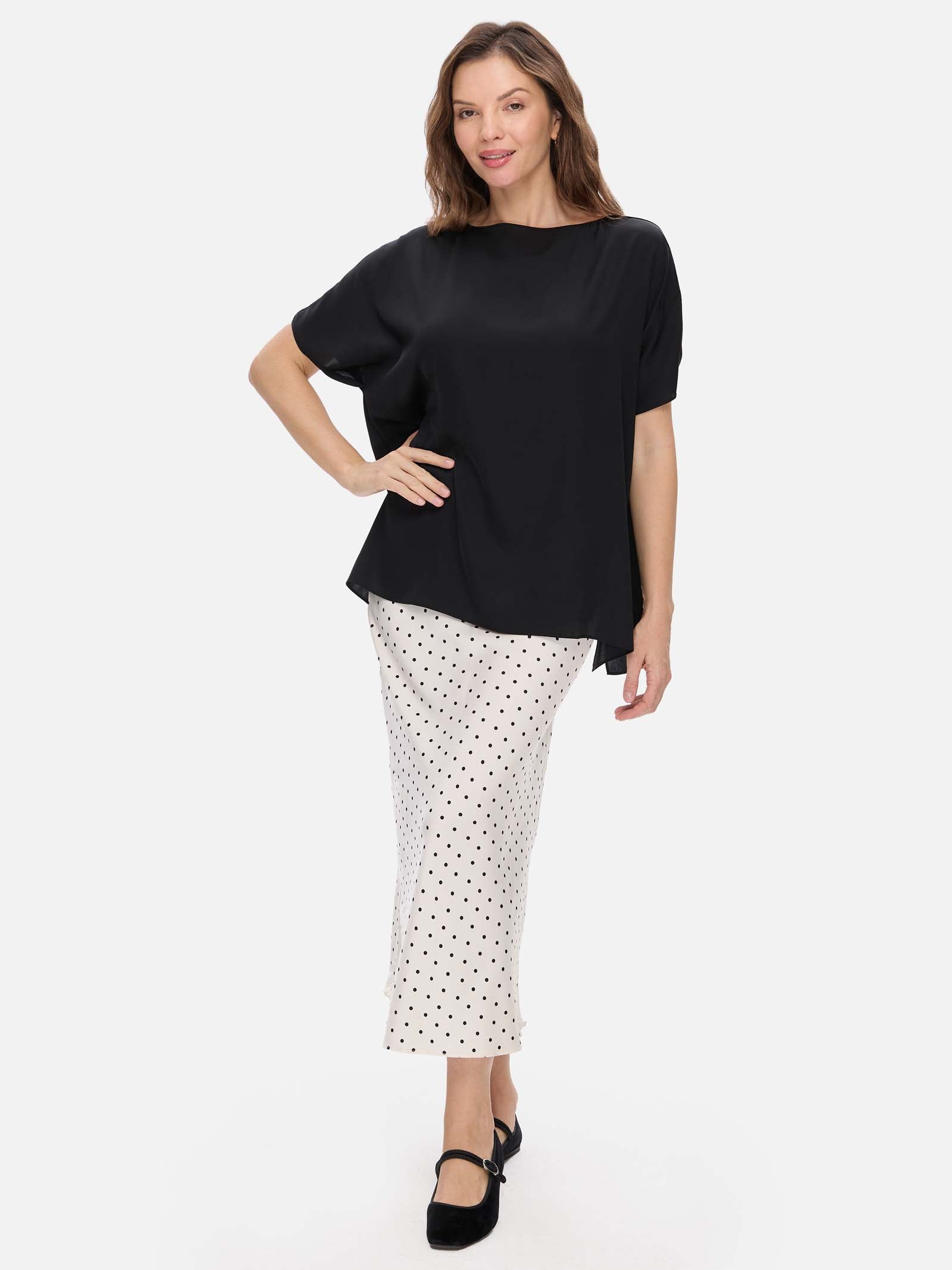 Woman wearing a black silk top and white polka dot skirt on a white background
