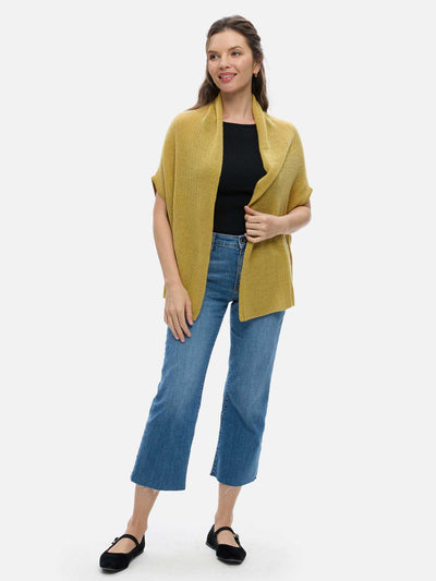 Woman wearing a mustard yellow cashmere vest, black top, and blue jeans on a white background