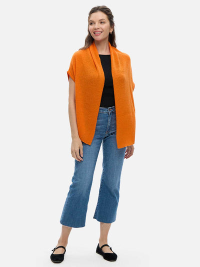 Woman wearing an orange cashmere vest over a black top and blue jeans on a white background