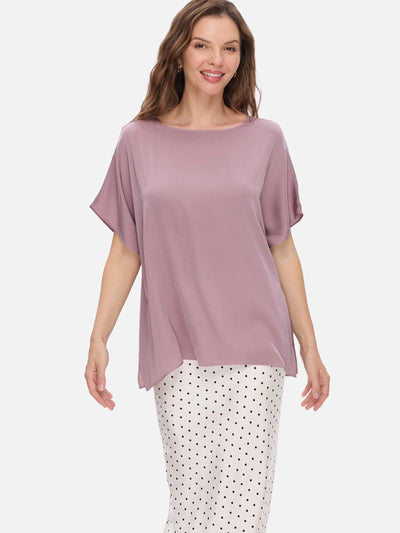 Woman wearing a mauve silk top and polka dot pants on a white background