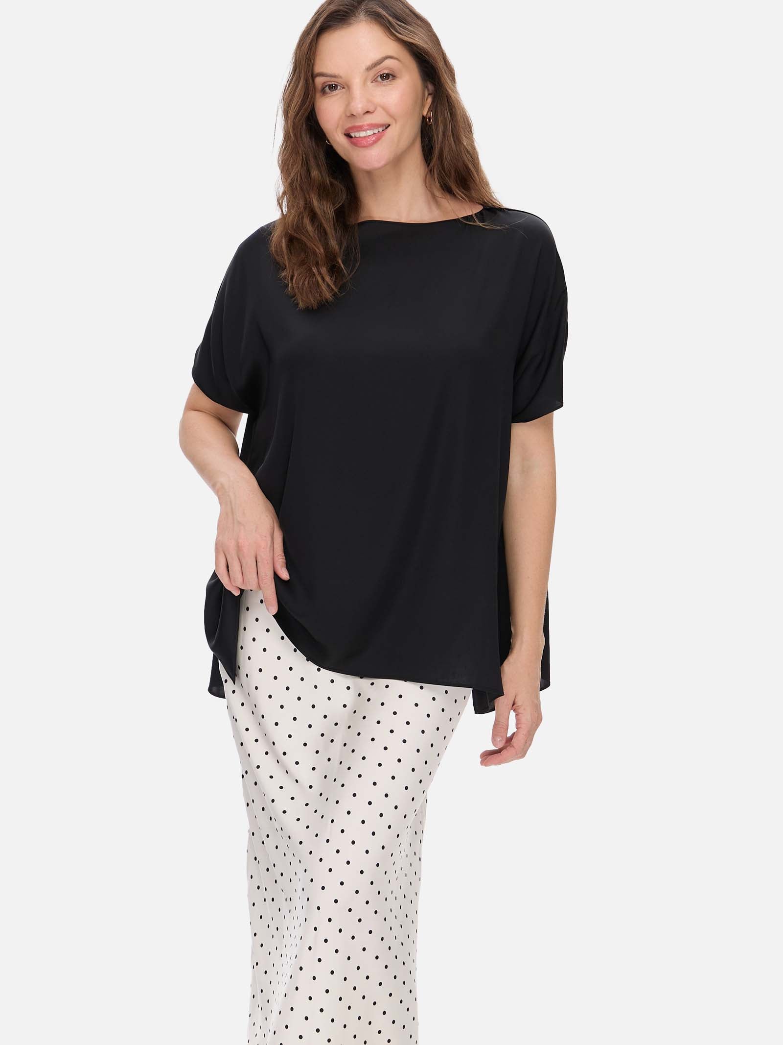 Woman wearing a black silk top and white polka dot pants on a white background