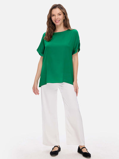 Woman wearing a green silk top and white pants on a white background
