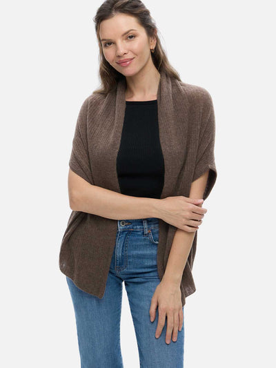 Woman wearing a brown cashmere vest over a black top and blue jeans on a white background