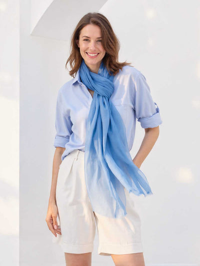 Woman wearing a light blue scarf and shirt with white shorts against a white background