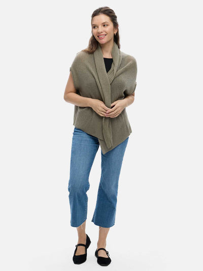 Woman wearing a green cashmere vest over a black top and blue jeans on a white background