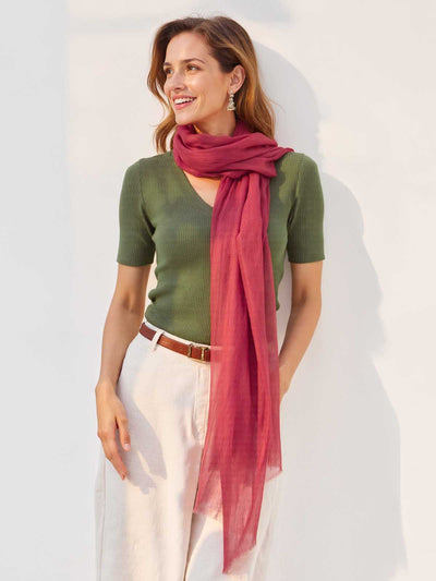 Woman wearing a green top and white pants with a red scarf on a light background