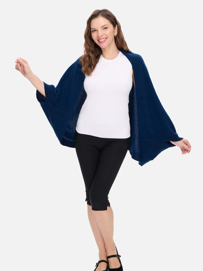 Woman wearing a navy blue cashmere wrap over a white top and black pants on a white background