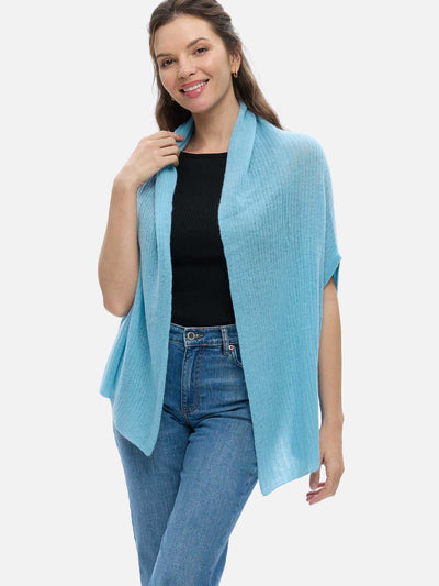 Woman wearing a light blue cashmere vest over a black top and jeans on a white background