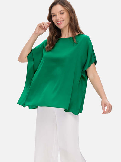 Woman wearing a green silk top and white pants on a white background