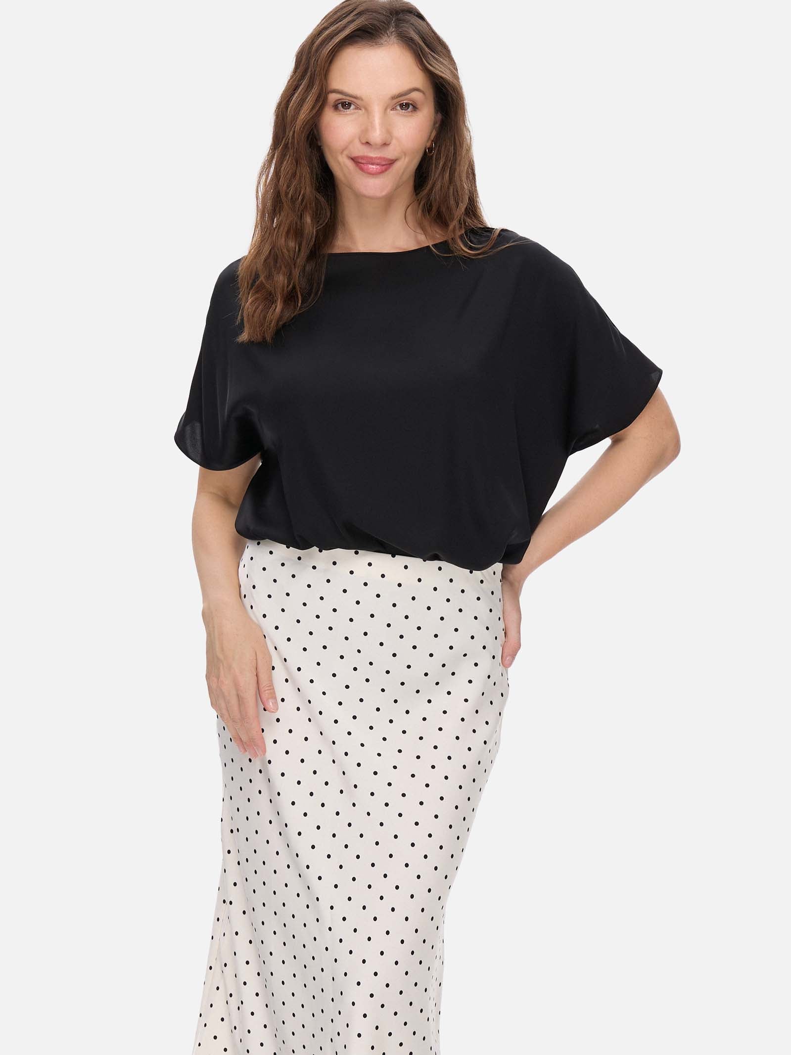 Woman wearing a black silk top and white polka dot skirt on a white background