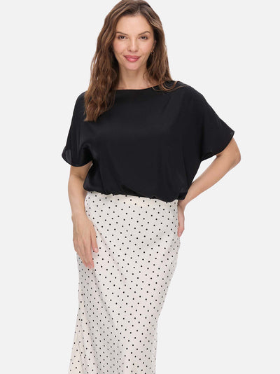 Woman wearing a black silk top and white polka dot skirt on a white background