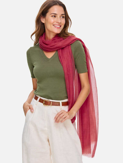 Woman wearing a green top, white pants, and a red scarf on a light gray background